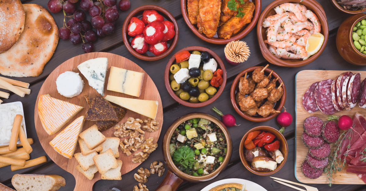 Table full of cheeses, cold meats, fruits, and bread.