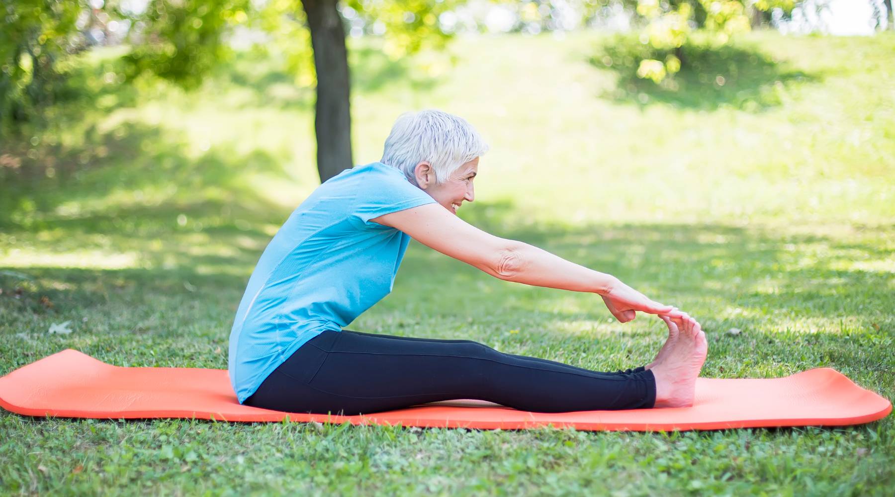 Senior woman stretching on a yoga mat at a park outdoors for joint health