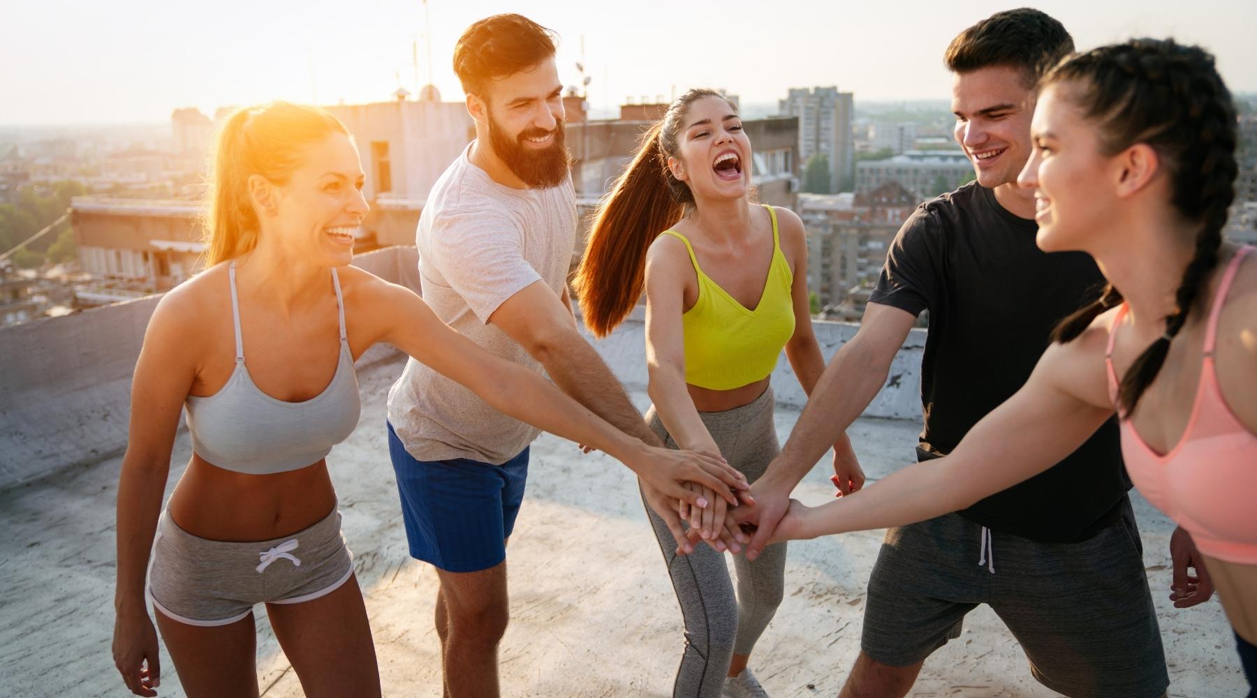 Group of young people in athletic clothes putting their hands together before a workout outdoors
