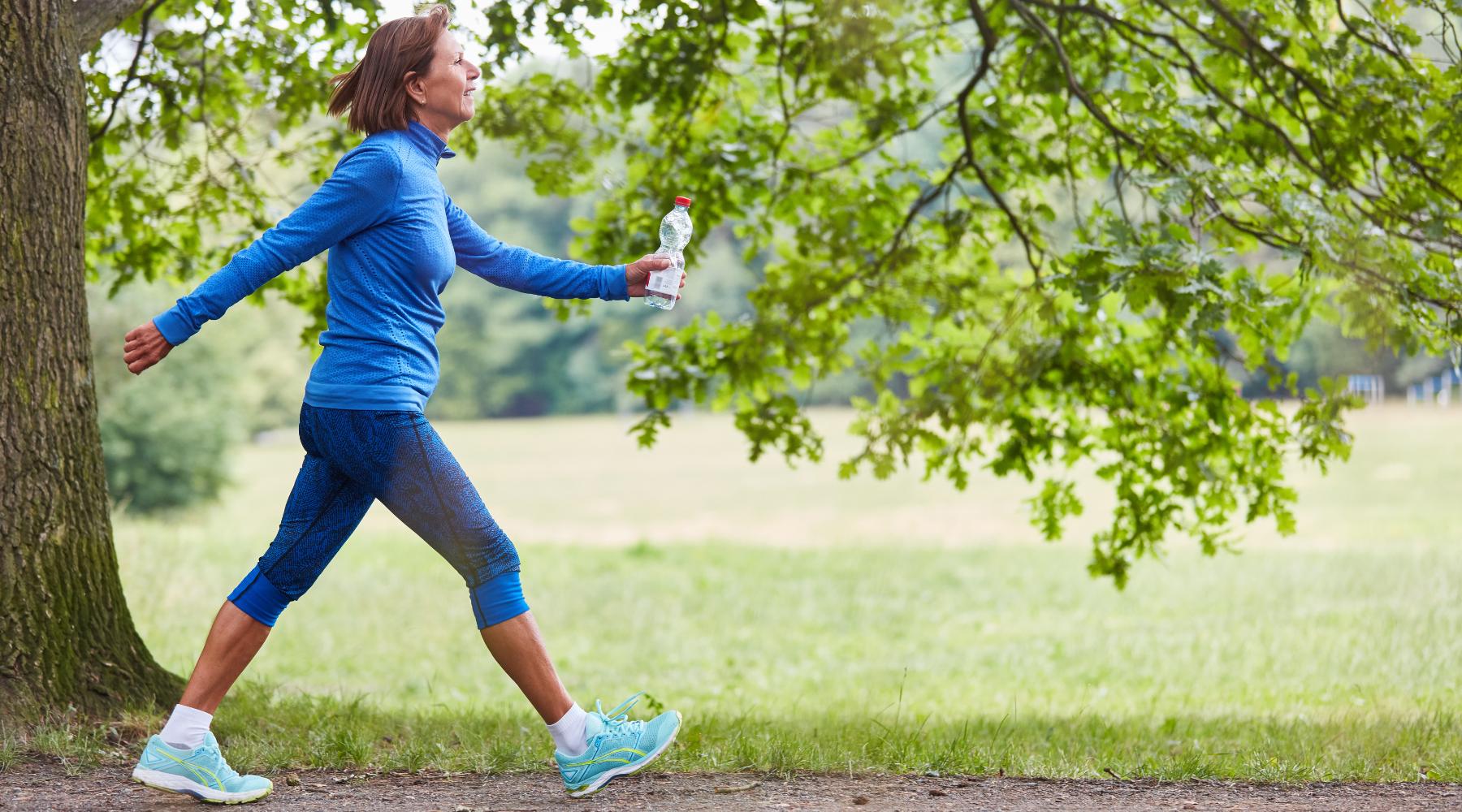 Woman walking outdoors for weight loss holding water bottle