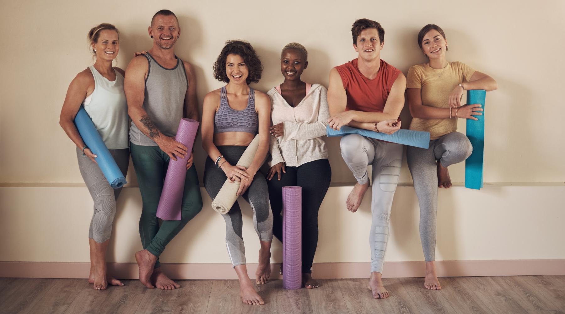 Group of young people holding yoga mats getting ready for pilates class