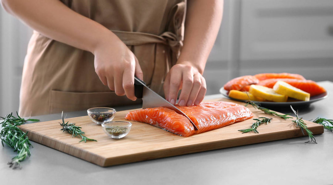 Young woman cutting fresh salmon fillet in kitchen meal prepping anti inflammatory diet