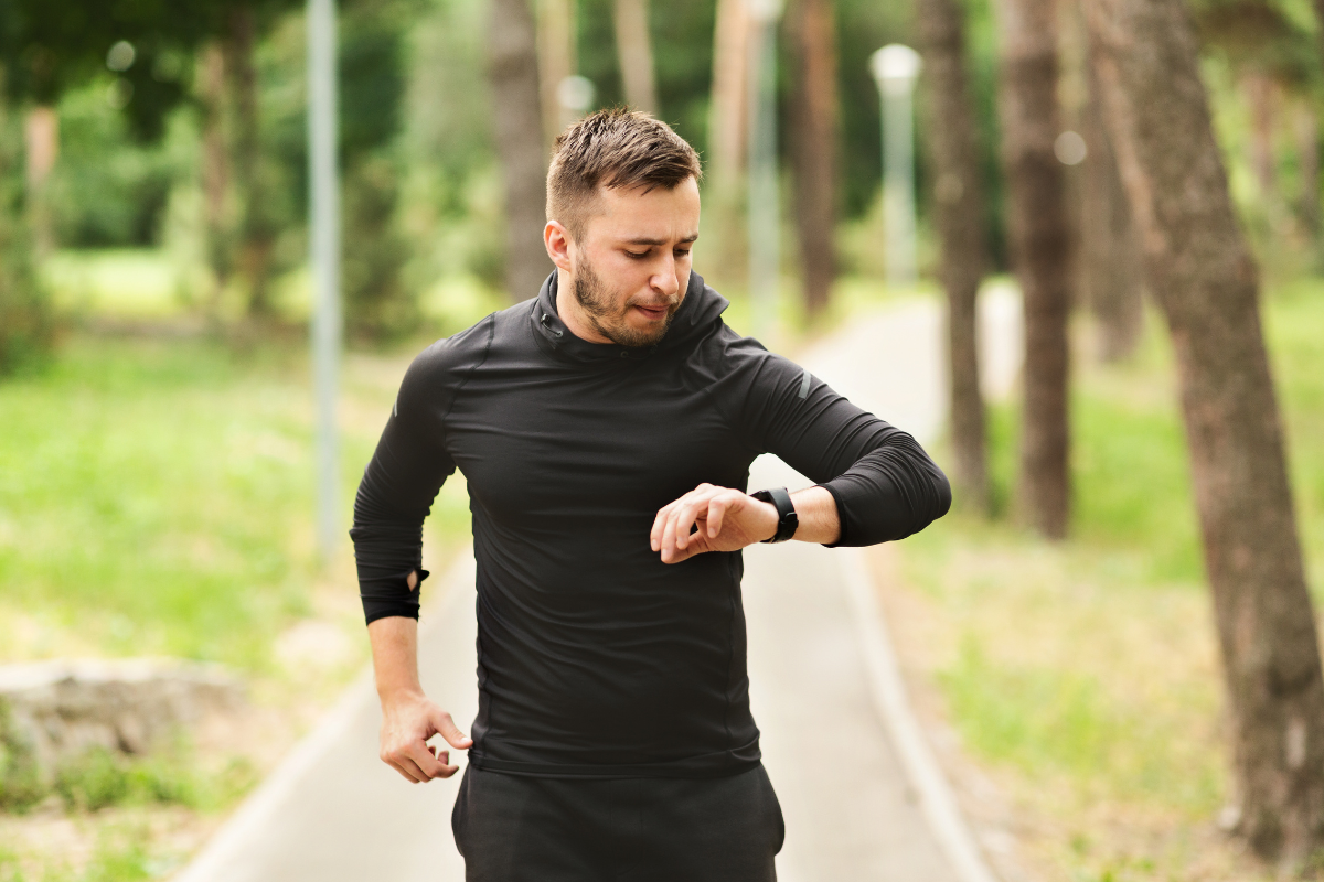 Man dressed in black running through a park, looking at his wrist activity tracker.