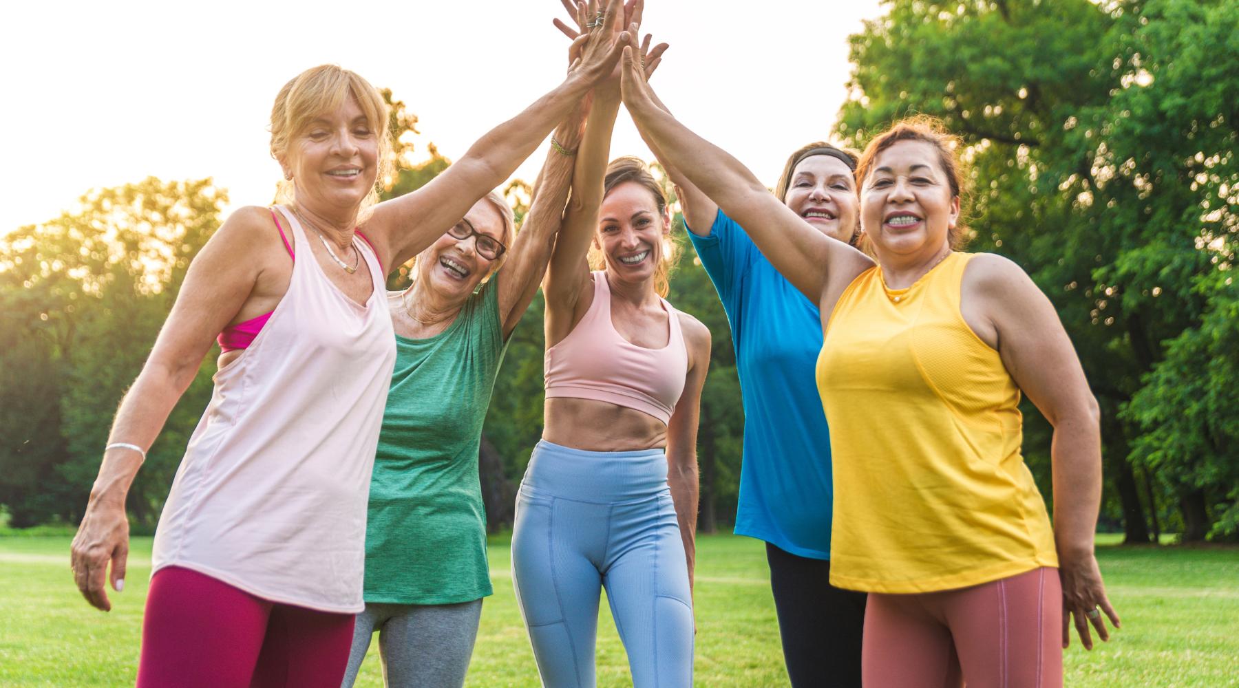Group of older women in athletic clothes high fiving outdoors after a workout