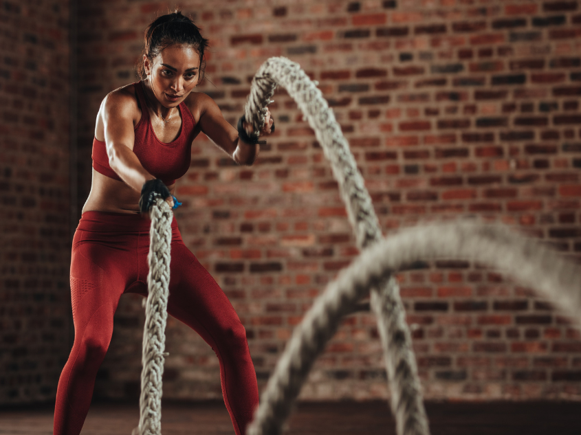 Athletic woman performing high-intensity interval training workout with battle rope