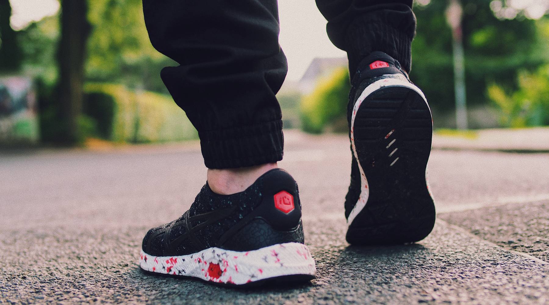 Close-up view of a person walking outdoors wearing black athletic sneakers with white and red accents, emphasizing movement and a healthy lifestyle.