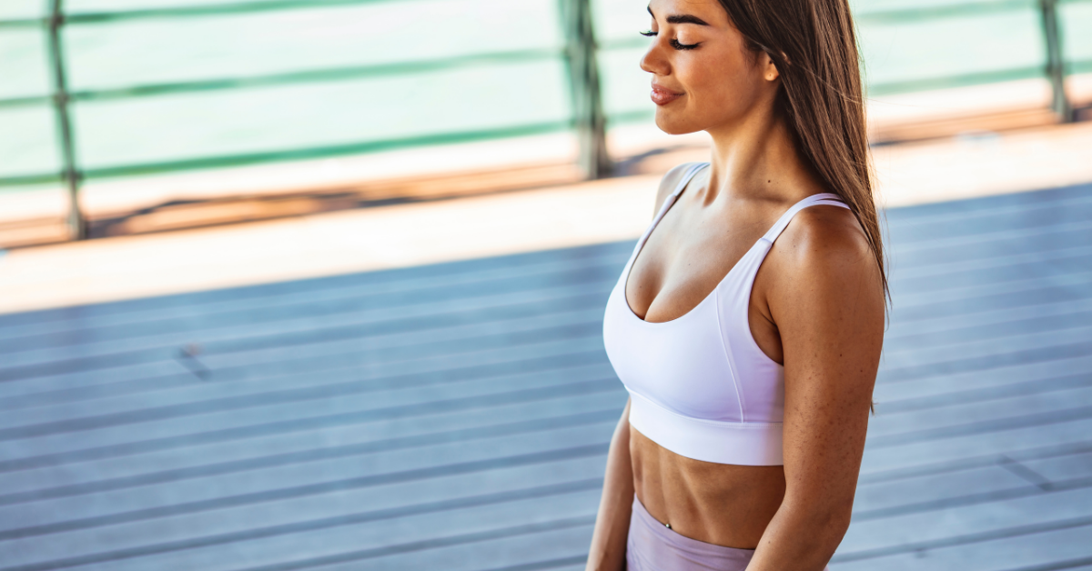 Fit woman in athletic clothes peacefully smiling outdoors with her eyes closed.