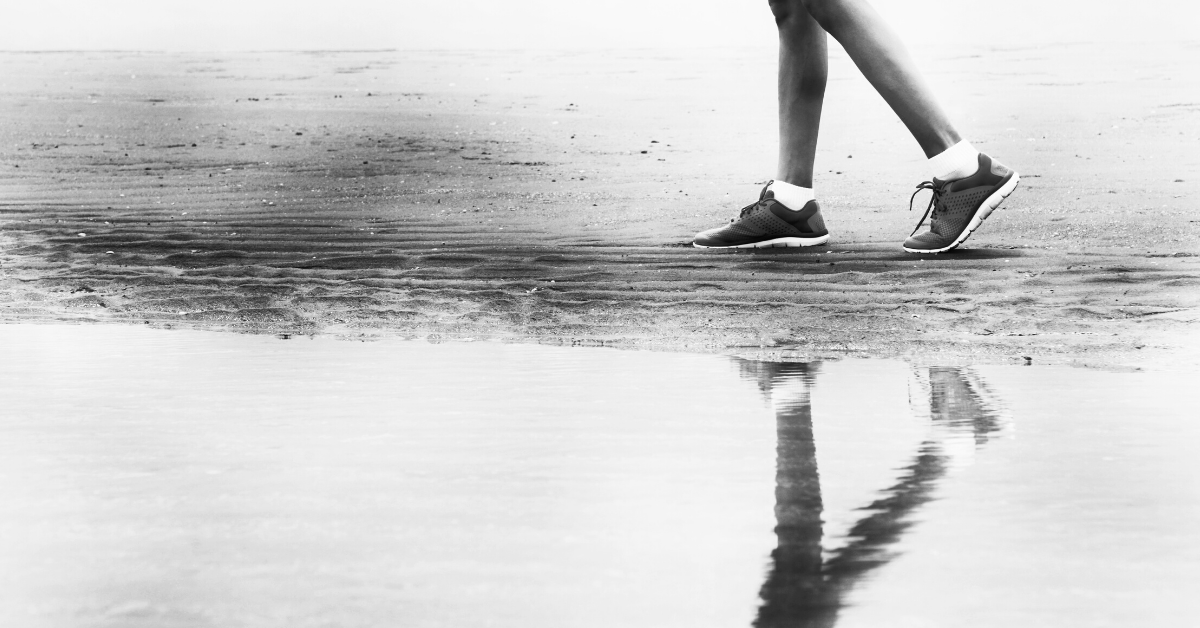 Black and white photo of person's legs while they take steps besides a large puddle.