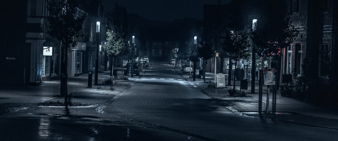 Empty suburban street at night, dimly lit by streetlamps.