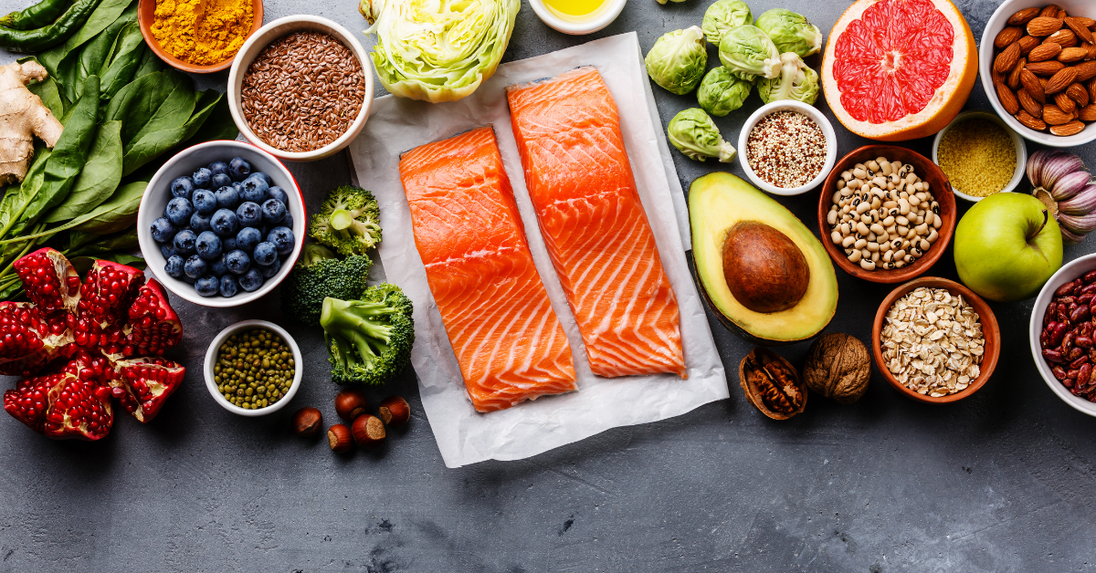 Overhead shot of uncooked salmon on a plate surrounded by several fruits and vegetables.