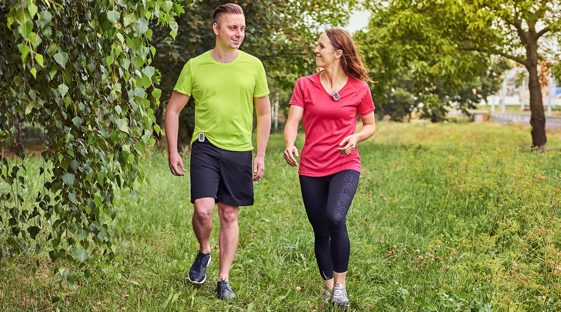 Young couple happily walking outdoors with 3DFitBud Pedometers clipped to their clothes
