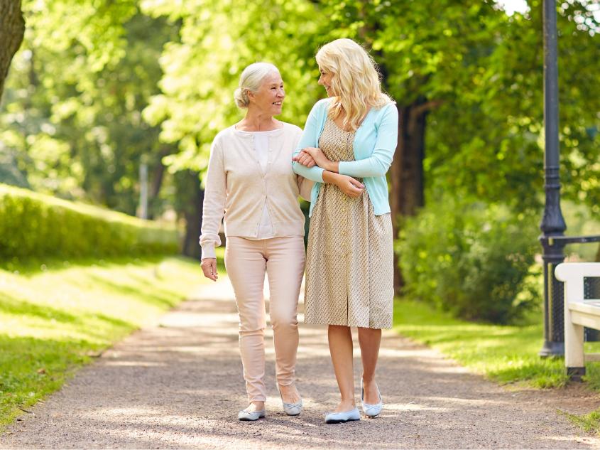 Elderly mother and young daughter walking in a park while linking arms