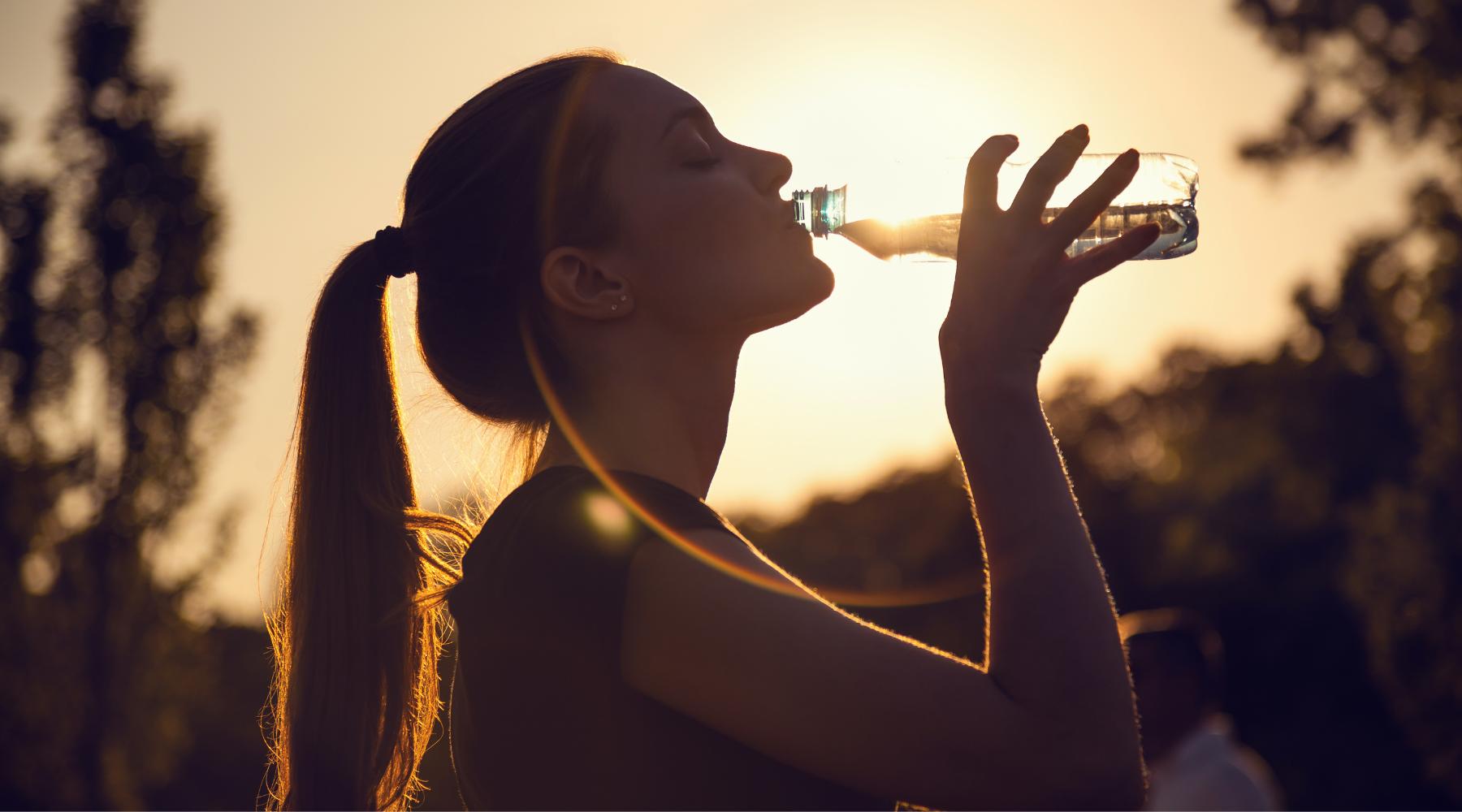 Woman drinking from water bottle with the sunset in the background