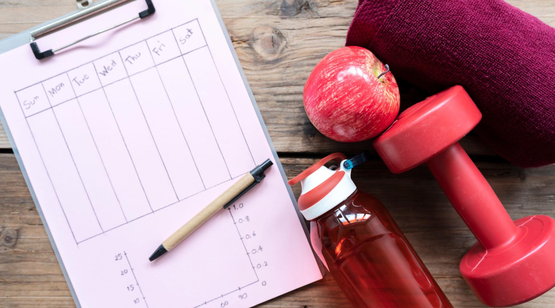Exercise plan next to red apple, water bottle, dumbbell, and gym towel