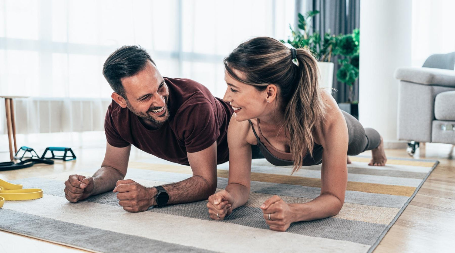 Young couple doing a plank exercise indoors while smiling