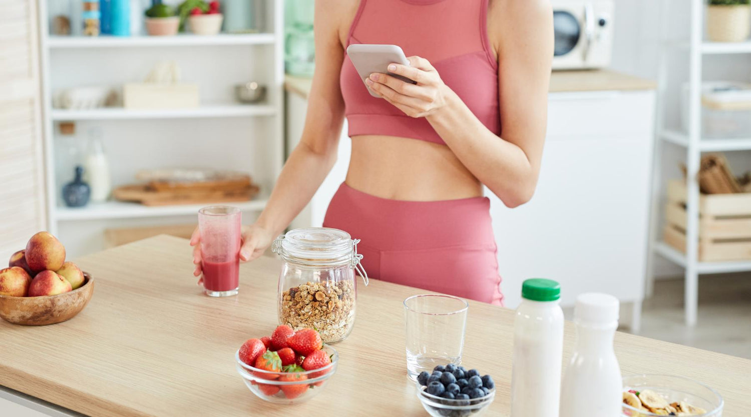 Athletic woman looking at the phone by the kitchen counter. Fruits. Healthy eating