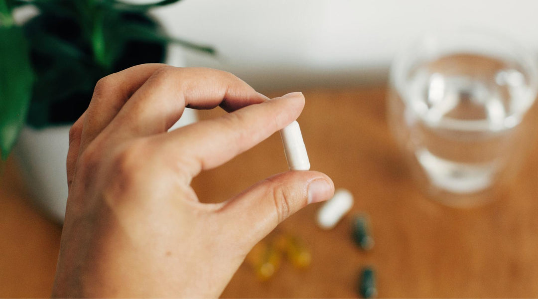 Hand holding magnesium capsule with glass of water in the background. Dietary supplementation. Magnesium glycinate.