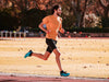 Man in orange t-shirt and black shorts running on a track field