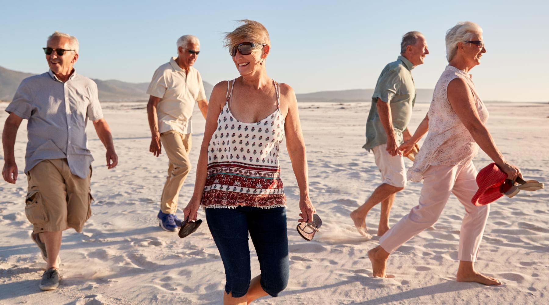 Group of elderly people having fun walking on the beach at sunset
