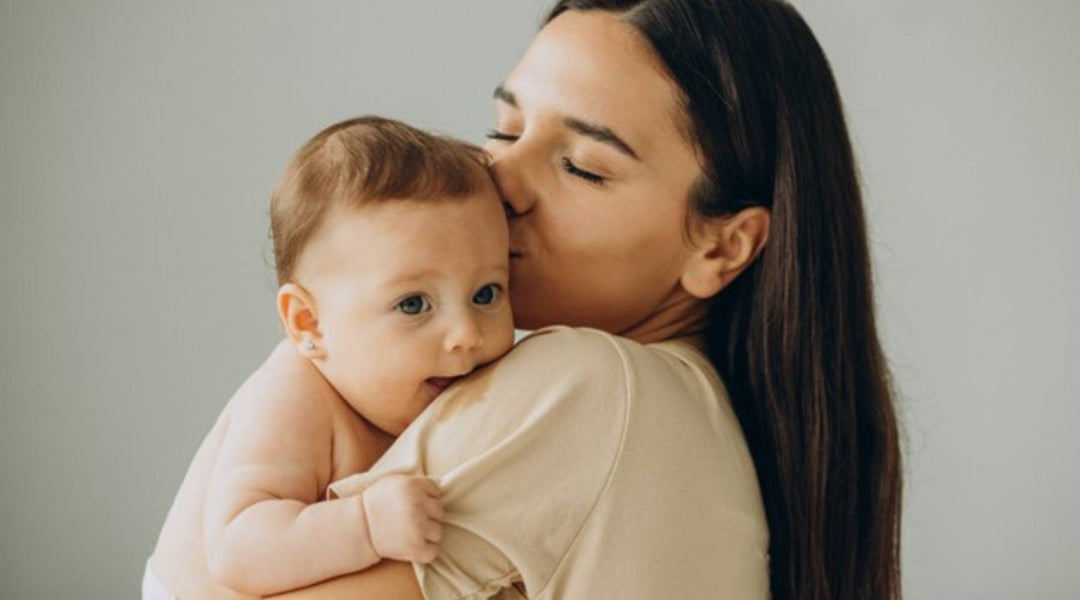 Mother gently kissing and holding her baby while bonding, symbolizing maternal love, health, and wellness during the nursing phase.