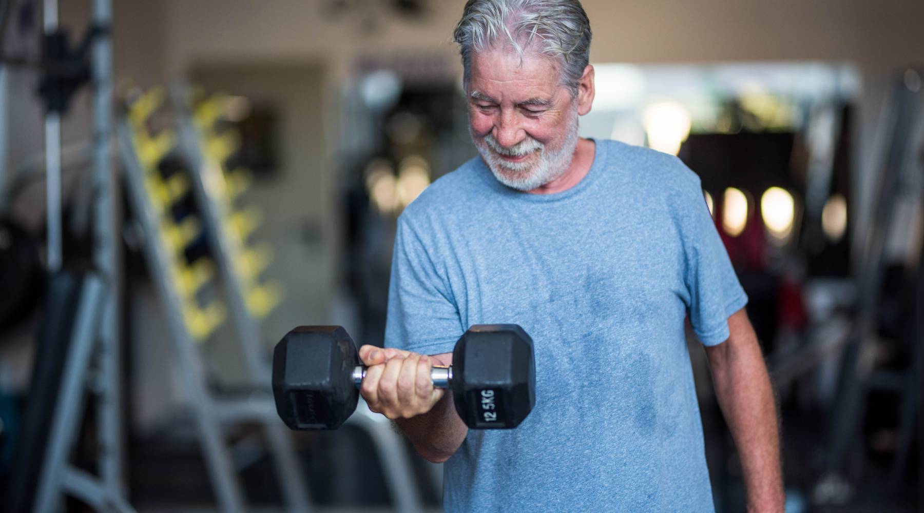 Senior man lifting heavy dumbbell at the gym strength training