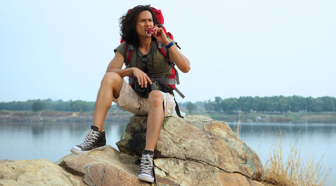 Fit woman in hiking gear taking a break during hike to eat protein bar at top of a hill overlooking lake