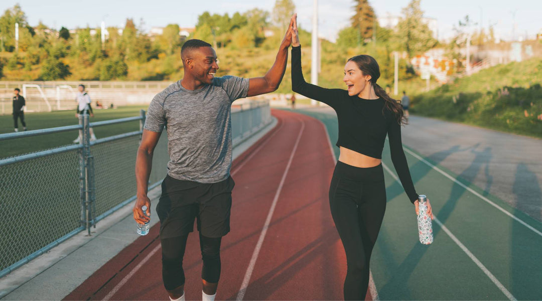 Two young fit friends high-fiving after walking workout on track field