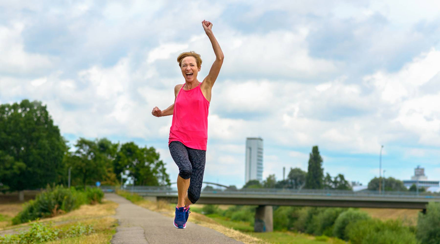 Woman in her 50s jumping energetically outdoors during a run