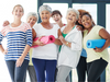 Group of seven older woman in casual clothes, smiling and holding yoga mats.