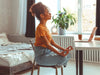 Woman sitting at a desk in her bedroom in a chair yoga meditation pose