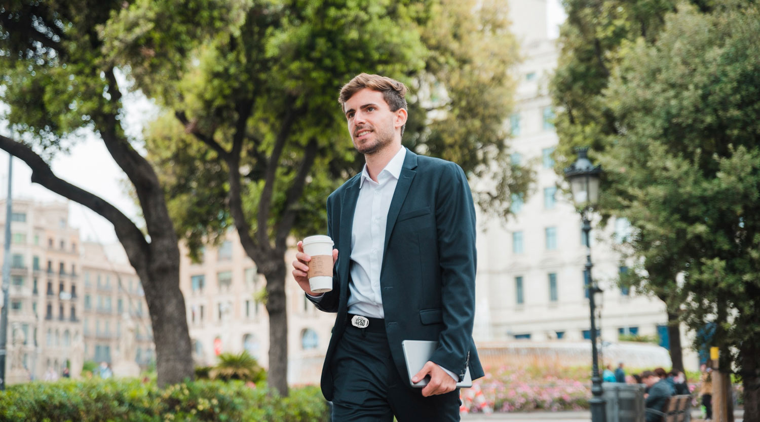 Walking workout for 30s & 40s - man in work clothes mid-stride on city sidewalk with 3DFitBud step counter clipped to hip, spring morning