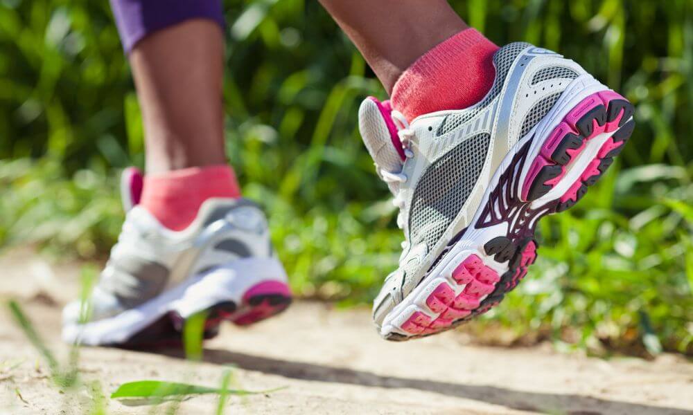 Close up of woman walking on dirt path with white, gray, and bright pink sneakers