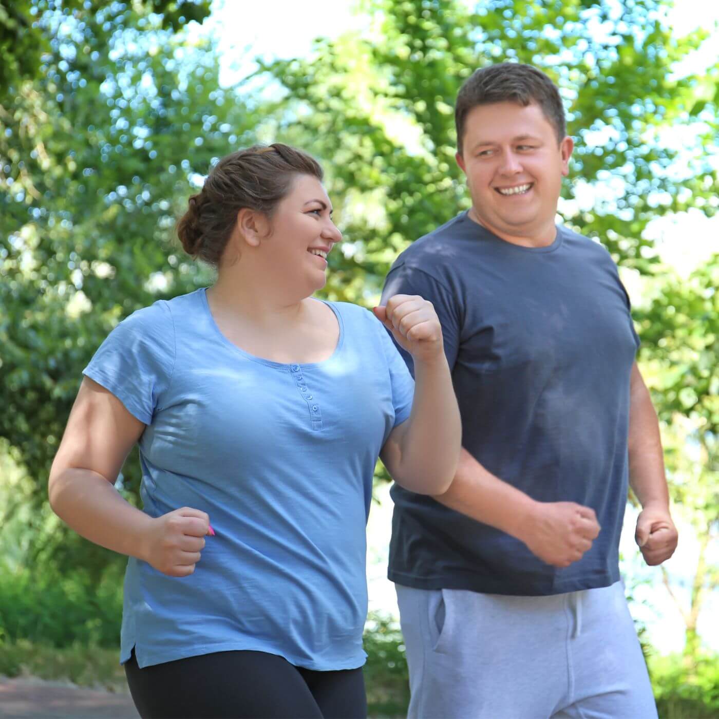 Overweight woman and man in blue shirts power walking in nature