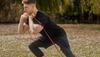Muscular man in black athletic clothes doing workout with red resistance band outdoors