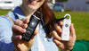 Smiling woman holding black Alarmee self defense keychain to the camera. Out of view woman holding white Alarmee to the right.